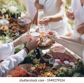hands with glasses of white wine or champagne. people raised their glasses at the picnic table. friends clinking glasses with wine - Shutterstock ID 1949279524