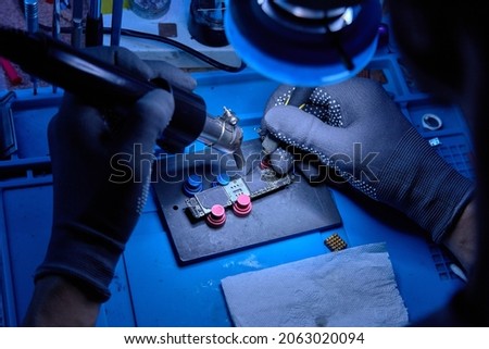 Hands in gloves of cellphone technology device maintenance engineer work on removing microprocessor from smartphone motherboard with knife and hot air heater. Close-up macro photo, Selective focus