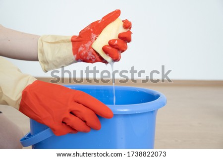 Hands in gloves for cleaning. A sponge with a detergent is foamed in a hand over a blue bucket.