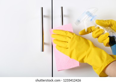 Hands in gloves with rag and bottle of detergent cleaning kitchen cabinet - Shutterstock ID 1233412426
