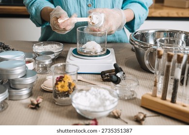 Hands in gloves scoop solid butter from jar into glass beaker on digital scale. raw beauty ingredients, skincare transparency trend, clean beauty formulation, botanical cosmetic actives.