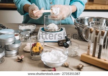 Hands in gloves scoop solid butter from jar into glass beaker on digital scale. raw beauty ingredients, skincare transparency trend, clean beauty formulation, botanical cosmetic actives.
