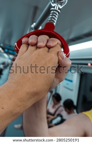 Hands gripping red train handle on crowded public transport journey.