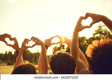 Hands Of Group Friends In The Shape Of A Heart Against The Sunset.