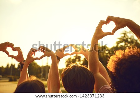 Hands of group friends in the shape of a heart against the sunset.