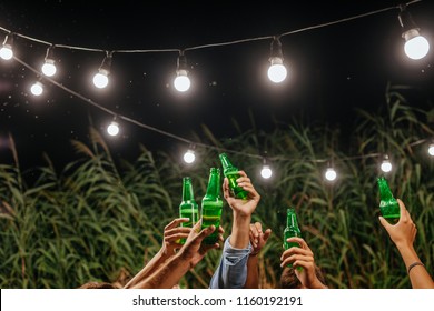 Hands Of Group Of Unrecognisable People Toasting With Beer Bottles At Outdoor Party.