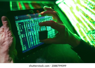 Hands of hacker with tablet computer and padlock on dark background