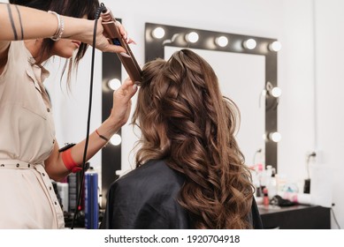 hands of a hairdresser with a Curling iron making a hairstyle for a curly girl in a professional beauty salon - Shutterstock ID 1920704918