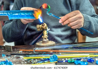 Hands of the handicrafts man making a glass subject at fair of crafts.Glass maker working melted glass with a flaming torch. Close up of flame from blowtorch on new glass art piece. - Powered by Shutterstock