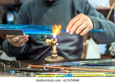 Hands of the handicrafts man making a glass subject at fair of crafts.Glass maker working melted glass with a flaming torch. Close up of flame from blowtorch on new glass art piece. - Powered by Shutterstock