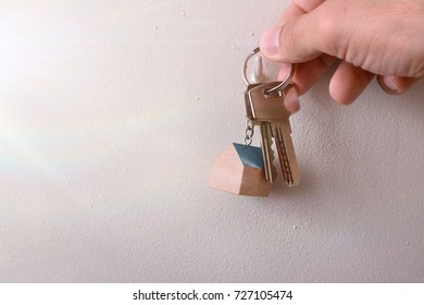 Hands Hanging Keys With Keyring On A Hook On The Wall Of A House With Sunshine