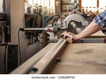 Hands Of Hard Working Woodworker Sawing A Piece Of Wood With A Mitre Saw In Woodworking Studio