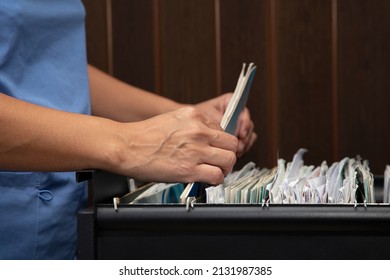 Hands Of Health Personnel Reviewing Files In The Filing Cabinet Of The Dental Office.