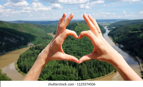 Hands heart gesture against panoramic summer view of the Saar river bend in Saarland, Germany. Saarschleife loop from the lookout point Cloef.

