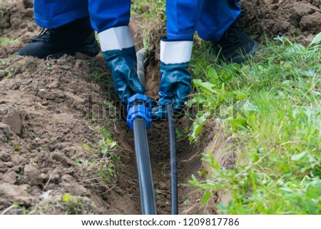 hands hold a black pipe over a dug hole in the ground