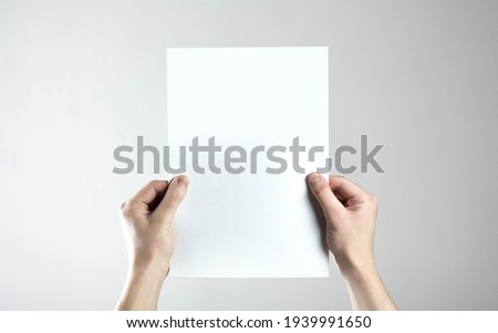 Hands hold an empty A4 sheet of paper. A clean flyer in your hands. For your text. Isolated on a gray background.