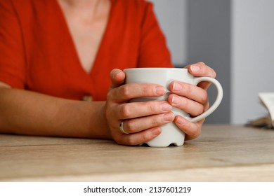 Hands hold a hot cup of coffee on a table, Female hands holding a cup of coffee with foam over red background, top view.