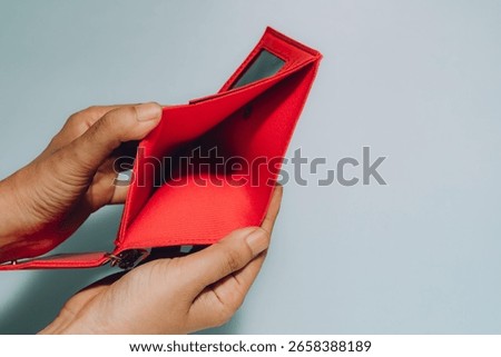 Hands hold an open, empty red wallet against soft blue. Conveys financial hardship, debt, budgeting, and the need for money management or saving.
