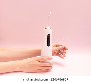 Hands hold oral teeth irrigator with nozzle pack, dental water tooth cleaner, white portable cordless water dental flosser on pink background. Waterproof home dental care device. Copyspace, horizontal - Shutterstock ID 2246786909