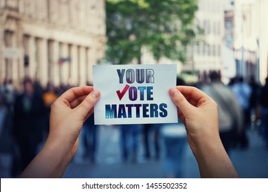 Hands hold a paper sheet with the message your vote matters over a crowded street background. People legal and democratic rights, every voice counts. Election campaign and electoral agitation concept. - Shutterstock ID 1455502352
