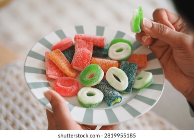 Hands hold a plate with different types of gummy candies.