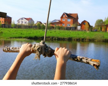 Hands Hold Rope Swing Before Jump Into The Water On The Lake And Mansion House Background