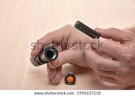 Hands hold a small black flashlight and replace the battery in it