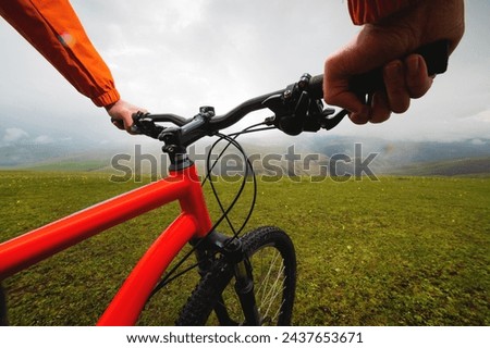 Hands hold the steering wheel of a bicycle while standing on a green meadow. A look through the eyes of a biker