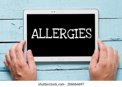 Hands hold tablet PC with text Allergies on wooden background