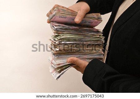 Hands hold tall stack of banknotes, symbol of finance growth and personal wealth. woman presents money pile, expressing economic success, profit and income power. Ukrainian currency is in female hands