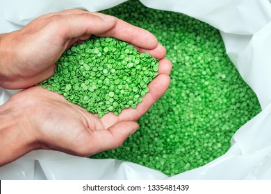 A hands hold or touching biodegradable plastic pellets, plastic polymer dye granules color clear green
