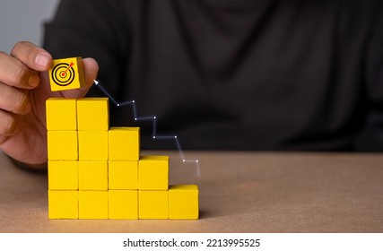 Hands hold a yellow wooden baton shaped like a virtual target and an arrow on the top screen. business success goals and objectives goal ideas - Powered by Shutterstock