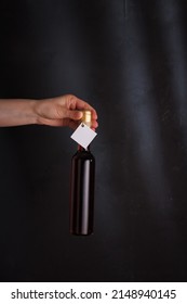hands holding 250 ml bottle of red wine with mock up label, no brand on black background. Cabernet sauvignon, merlot, pinot noir. Alcohol drink, copy space