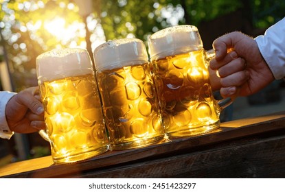 hands holding bavarian beer mugs with sunlight from the background on a wooden table in Beer garden or oktoberfest in Germany - Powered by Shutterstock