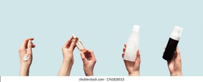 Hands Up Holding Beauty Cosmetic Products Isolated On Blue Background Horizontal Banner Format. Woman Takes Oil Serum, Toner Or Tonic Bottle, Facial Foam Cleanser And Smear Smudge Moisturizer Cream