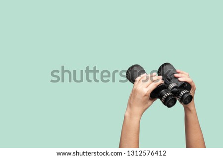 Hands holding binoculars on green background, looking through binoculars, journey, find and search concept.