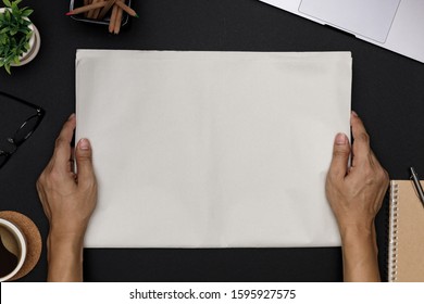 Hands Holding Blank Business Newspaper And Office Supplies With Notebook, Hot Coffee Cup, Glasses, Books And Accessories On Black Desk Topview, Daily Newspaper Mockup Concept