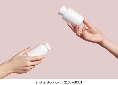 Hands holding blank white plastic tubes on pink background. Packaging for pills, capsules or supplements. Medic product branding mockup. High quality photo