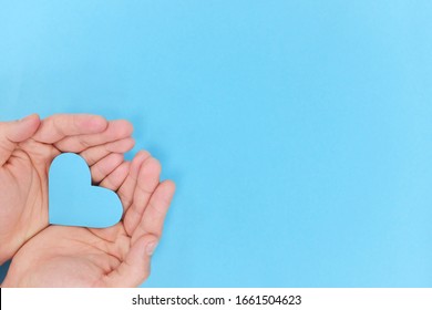 Hands holding a blue heart shape in light blue background. Top view with copy space. - Shutterstock ID 1661504623