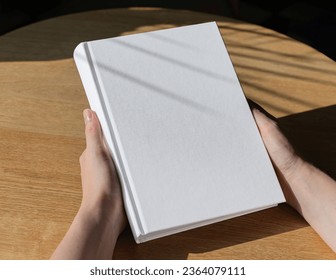 Hands holding book in hard cover mock up on wood table