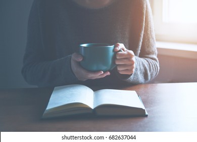 hands holding book and reading with cup of coffee or tea