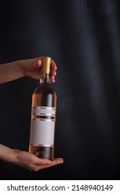 hands holding bottle of pink wine with mock up label, no brand on black background. pinot noir. Alcohol drink, copy space