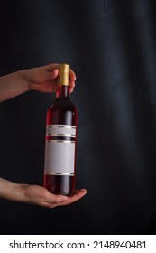 hands holding bottle of pink wine with mock up label, no brand on black background. pinot noir. Alcohol drink, copy space