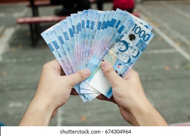 Hands holding a bunch of 1000 Philippine peso cash spreading it like a fan shape