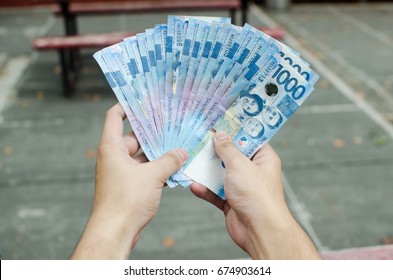 Hands holding a bunch of 1000 Philippine peso cash spreading it like a fan shape