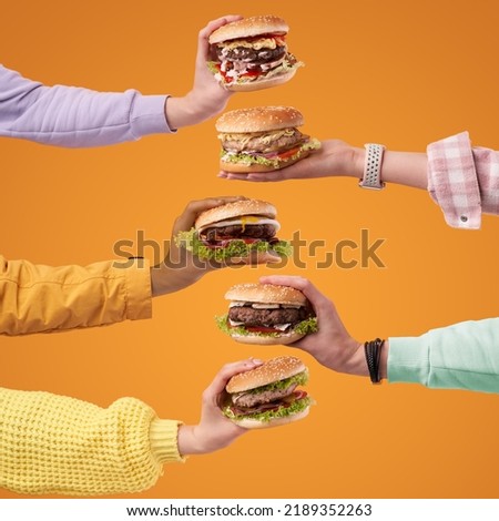 Hands holding burgers on the orange background. Burger with juicy marbled beef patty, freshly baked bun, fresh farm vegetables, melting cheese and signature sauce.