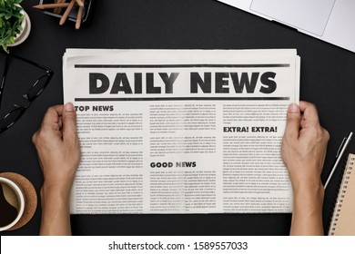 Hands Holding Business Newspaper And Office Supplies With Notebook, Hot Coffee Cup, Glasses, Books And Accessories On Black Desk Topview, Daily Newspaper Mockup Concept