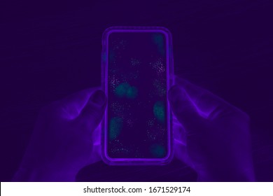 Hands holding cell phone with dirty contaminated touch screen - UV Blacklight exposing infectious bacteria and harmful germs on mobile smartphone display -  Disease, corona virus and hygiene concept