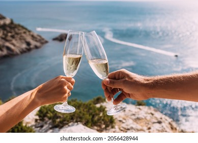Manos sosteniendo gafas de champán sobre el mar. Unas vacaciones románticas. Dos manos con gafas de champán al fondo del mar. Una pareja enamorada bebe champán a orillas del mar. Copiar espacio