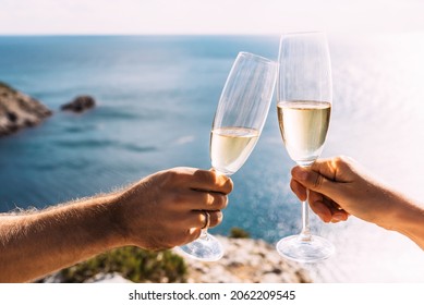 Hands holding champagne glasses over the sea. Romantic vacation. Two hands holding champagne glasses on the background of the sea. Toast with champagne glasses on the seashore. Copy space - Powered by Shutterstock